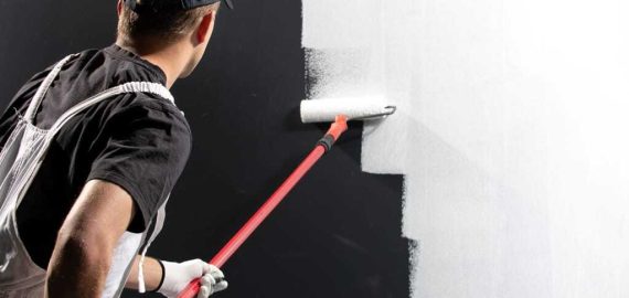Male decorator painting a wall with white color